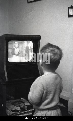 Fine del 1950s, storico, un ragazzino vicino ad un piccolo televisore dell'epoca che guarda un programma, Inghilterra, Regno Unito. Nel 1950, un televisore era un prodotto di lusso, con solo circa 350.000 famiglie britanniche in possesso di un televisore, ma alla fine del decennio quasi il 75% della popolazione aveva la televisione. Foto Stock