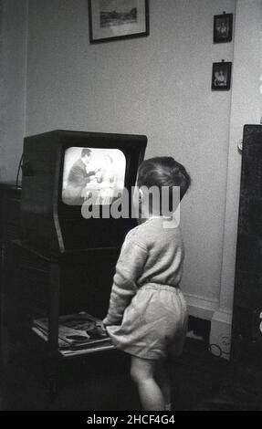 Fine 1950s, storico, un ragazzino che si alza vicino ad un piccolo televisore dell'epoca che guarda un programma, Inghilterra, Regno Unito. Nel 1950, un televisore era un prodotto di lusso, con solo circa 350.000 famiglie britanniche in possesso di uno, ma alla fine del decennio quasi il 75% della popolazione aveva la televisione Copie della popolare rivista femminile, 'Donna' si trovano sotto la TV. Foto Stock