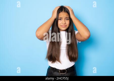 Ritratto di preoccupata ragazza preoccupato in bianco t-shirt guardare fotocamera mettere le mani sulla testa isolato su sfondo blu. Foto Stock