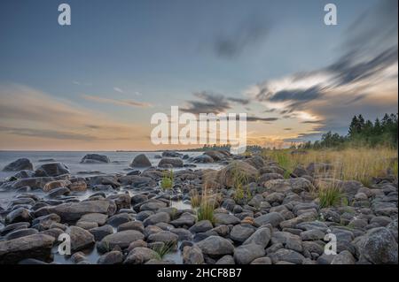 Lunga esposizione di un magnifico tramonto morbido e colorato vicino alla pietra del mare. Bel movimento nube con pietre di mare. Foto Stock