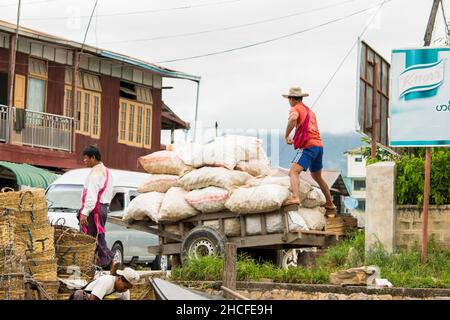 Uomini birmani che caricano e scaricano sacchi di forniture e cibo dalle barche ai carrelli, nel lago Inle Foto Stock