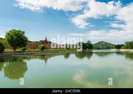 Una grande piscina d'acqua riflettente, con una vista distante della collina di Mandalay, contro il cielo blu e nuvoloso Foto Stock