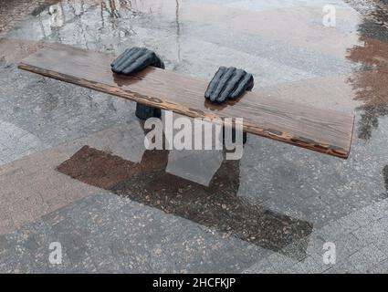 Panca decorativa fatta a mano sulla strada sotto forma di due mani che reggono una tavola di legno. Sul marciapiede in cemento Foto Stock