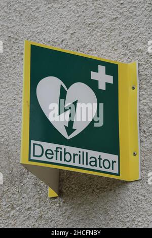 Segnale informativo per l'apparecchiatura del defibrillatore cardiaco. Cartello bianco e verde su sfondo giallo, montato su parete color crema. Foto Stock
