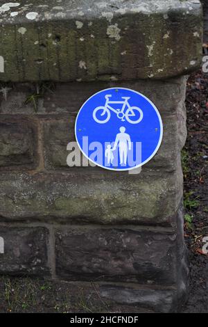 Pista ciclabile e pedone segnaletica stradale su muro di pietra. Grande cartello circolare blu rotondo con bici isolata e genitore con bambino. Foto Stock