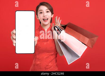 Felice anno nuovo cinese. Felice giovane donna che mostra lo schermo bianco dello smart phone e le borse di shopping Foto Stock