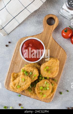 Pepite di pollo dorate in un asse di legno, cosparse di cipolle verdi e un ketchup. Superficie piana Foto Stock