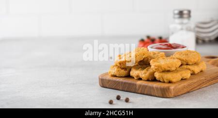 Pepite di pollo dorate in un asse di legno, cosparse di cipolle verdi e un ketchup. Spazio di copia. Foto Stock