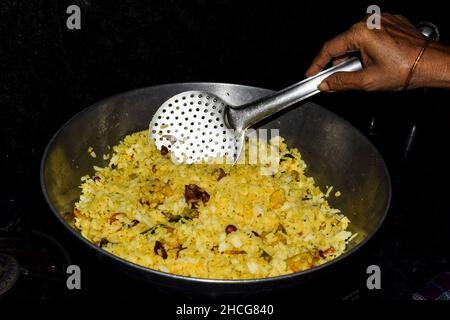 Donna che cucina deliziosa Kanda poha, maharastrian piatto in casa cucina. Riso sbattuto bianco ammollato e cipolle fritte, peperoncino verde, foglie di curry, turme Foto Stock