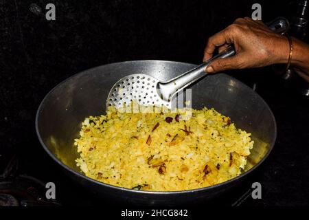 Donna che cucina deliziosa Kanda poha, maharastrian piatto in casa cucina. Riso sbattuto bianco ammollato e cipolle fritte, peperoncino verde, foglie di curry, turme Foto Stock