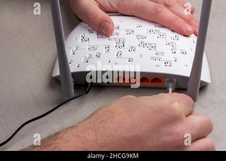 Le mani maschio collegano i cavi a un nuovo router Wi-Fi bianco con antenne grigie in primo piano Foto Stock