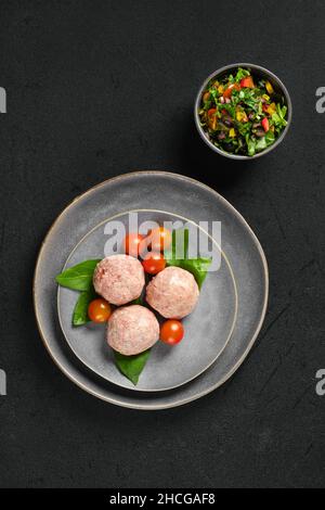 Vista dall'alto di polpette di vitello surgelate semilavorate su un piatto con basilico e pomodoro Foto Stock