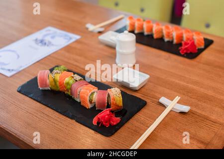 piatti neri con panini di sushi tradizionali vicino a bacchette, set di salsa di soia e menu sfocato sul tavolo nel sushi bar Foto Stock