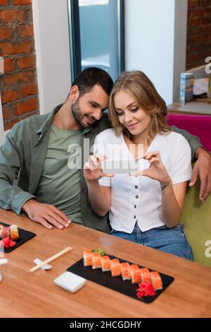 donna che scatta foto di sushi rotola sullo smartphone vicino a un ragazzo sorridente Foto Stock