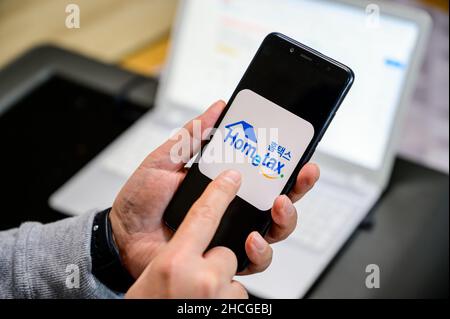 Seoul, Corea del Sud - 29 dicembre 2021: La mano di un uomo che installa un'app per smartphone per l'adeguamento fiscale di fine anno. Foto Stock