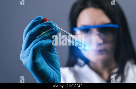 Lavoratore di laboratorio medico femminile con provetta per analisi di Coronavirus 2019-nCoV. Campione di sangue positivo nella mano dello scienziato. Interruzione del coronavirus Foto Stock