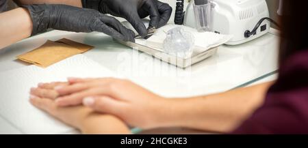 Mani in guanti neri di manicurista preparazione di speciale lima per unghie per trattamento manicure in un salone di bellezza Foto Stock