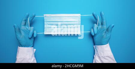 Il medico ha le mani nei guanti mostrando la maschera medica viso su sfondo blu. Misure preventive per la protezione contro l'infezione da virus di Corona Covid-19. Foto Stock