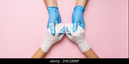 Le mani del medico nei guanti che tengono le mani della donna nei guanti. Banner medico con spazio per la copia su sfondo rosa. Immagine del concetto di cura Foto Stock