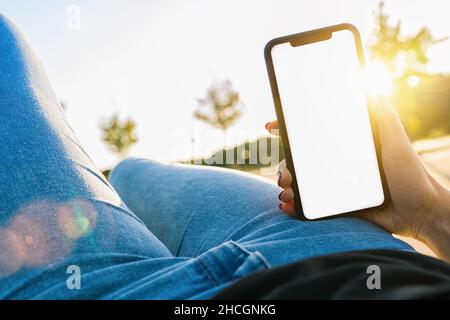 Immagine mockup delle mani che tengono il telefono cellulare nero con lo schermo vuoto del desktop in estate Foto Stock