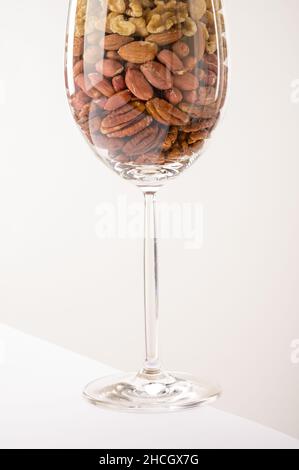 Vaso di vetro riempito con una varietà di nutrizione e snack sani e noci su uno sfondo bianco Foto Stock