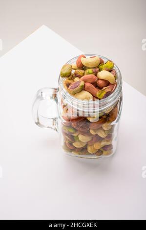 Vaso di vetro riempito con una varietà di nutrizione e snack sani e noci su uno sfondo bianco Foto Stock