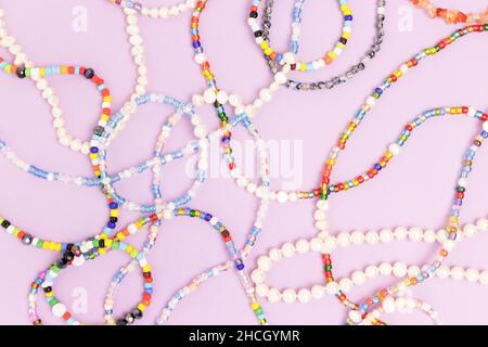 Collane e bracciali realizzati con perle e perle colorate su sfondo viola. Foto Stock