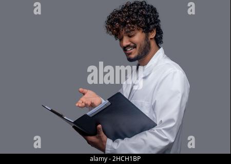 Sorridente medico scrutando i documenti nelle sue mani Foto Stock