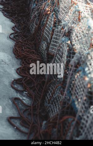 Vista verticale di varie trappole per la pesca in metallo e corde sparse. Vista ravvicinata della gabbia di granchio impilata sul pavimento di un molo da pesca. Impilare l'aragosta o. Foto Stock