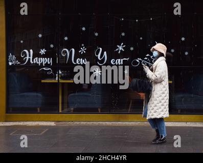 Londra, Regno Unito 29th dicembre 2021. Una donna cammina davanti a un cartello "Happy New Year" sulla finestra di un ristorante chiuso nel West End di Londra. Nonostante la mancanza di nuove restrizioni, molti ristoranti hanno segnalato un calo dei clienti a causa della diffusione della variante Omicron del coronavirus. Credit: Vuk Valcic / Alamy Live News Foto Stock