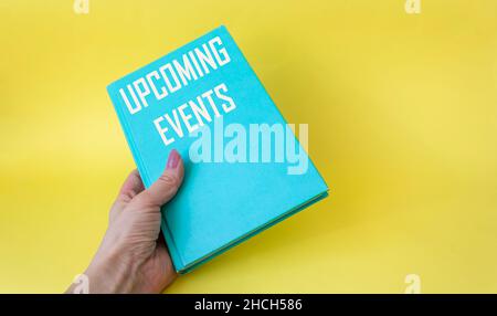 Donna mano tenendo verde diario con il testo segno che mostra prossimi eventi su sfondo giallo.Conceptual foto di prossimo pianificato pubblico o sociale anche Foto Stock