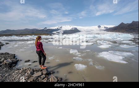 Donna di fronte alla laguna di ghiaccio Fjallsarlon, ghiaccio galleggianti di fronte al ghiacciaio Vatnajoekull, Hornafjoerour, Islanda Foto Stock