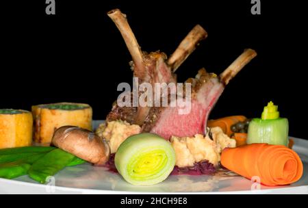 Sella di agnello arrosto rosa su polenta di mais con cipolle rosse e verdure varie, fotografia da studio con sfondo nero Foto Stock