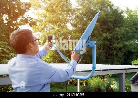 Un tecnico asiatico anziano del satellite sta regolando l'antenna parabolica su un segnale adatto per ricevere i segnali televisivi a casa. Foto Stock