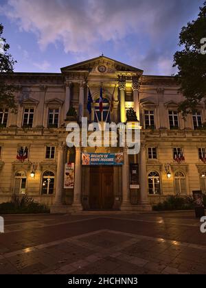 Vista frontale dello storico municipio di Avignone, Provenza, Francia in serata con facciata illuminata, bandiere e alberi in autunno. Foto Stock