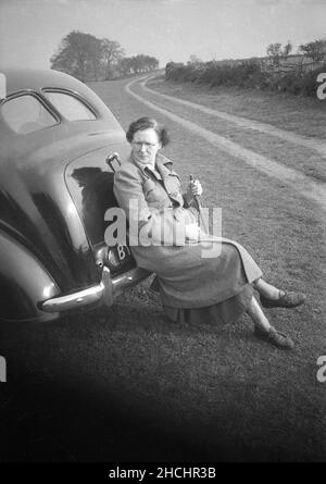 1950s, storico, fuori in un campo di contea, una signora camminatore poggiato sul paraurti di metallo di una macchina dell'epoca, appoggiata contro il suo stivale piatto, Inghilterra, Regno Unito. Foto Stock