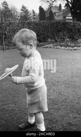 Fine 1950s, storico, all'aperto in un giardino, un ragazzino in un maglione di lana e pantaloncini che giocano con un giocattolo da spining portatile, Inghilterra, Regno Unito. Foto Stock