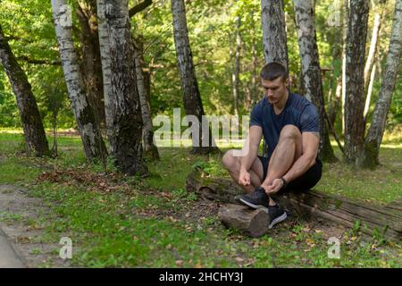 L'uomo che lega le sue scarpe nel parco all'aperto, intorno alla foresta, querce verde erba verde giovane atleta resistente atleta. Runner esercizio, lifestyle voi Foto Stock