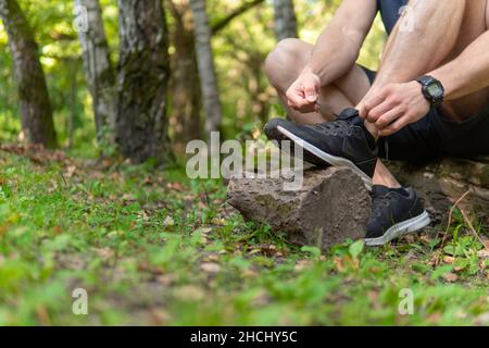 Uomo che lega le sue scarpe nel parco all'aperto, intorno alla foresta, querce erba verde giovane atleta di perseverante atleta atletica. Esegui esercizio sportivo, fitness tr Foto Stock