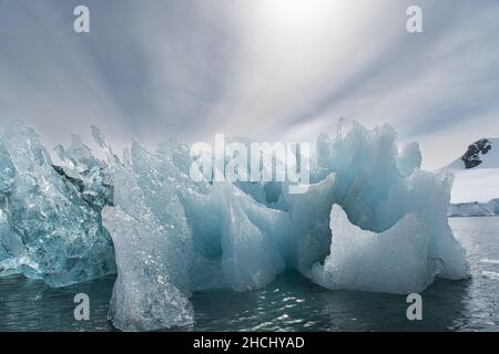 Una foto di un iceberg retroilluminato che mostra ghiaccio chiaro, blu e nero con sfondo montagna in Paradise Bay, Antartide Foto Stock