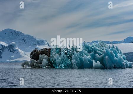 Una foto di un iceberg che mostra ghiaccio chiaro, blu e nero con sfondo montagna in Paradise Bay, Antartide Foto Stock