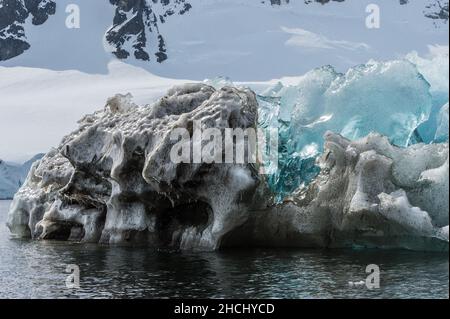 Una foto di un iceberg che mostra ghiaccio chiaro, blu e nero con sfondo montagna in Paradise Bay, Antartide Foto Stock
