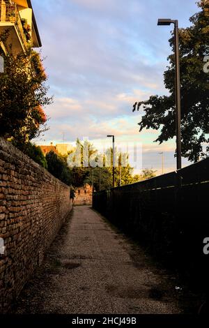 Vicolo tra un muro di mattoni e una recinzione al tramonto Foto Stock