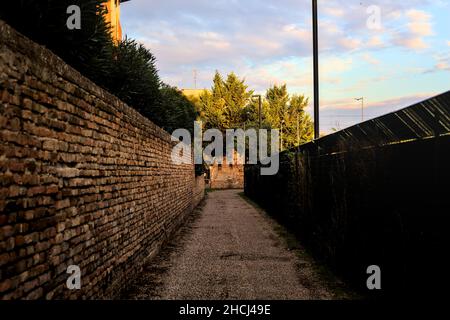 Vicolo tra un muro di mattoni e una recinzione al tramonto Foto Stock