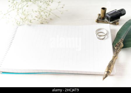 Alcuni anelli di cerimonia nuziale o di aggancio con una vecchia penna e carta per scrivere una nota. I fiori belli accompagnano la composizione. Concetto di amore, copia spac Foto Stock