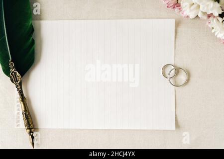 Alcuni anelli di cerimonia nuziale o di aggancio con una vecchia penna e carta per scrivere una nota. I fiori belli accompagnano la composizione. Concetto di amore, copia spac Foto Stock