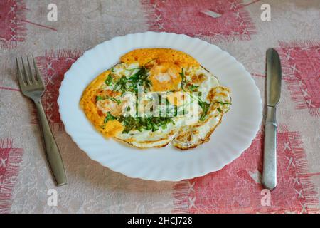 Sana prima colazione, uova fritte e verdure verdi in piastra di ceramica bianca, servita sul tavolo con posate Foto Stock