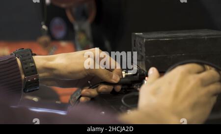 Vista laterale di una mano che inserisce un filo nell'interruttore. Primo piano del processo di impostazione del suono, mani maschili che regolano i comandi dell'attrezzatura professionale Foto Stock