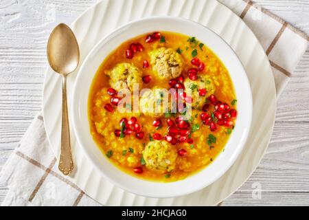 Anar di Ash-e, zuppa invernale di melagrana gialla in due pezzi con polpette, zuppa spessa, in una ciotola bianca su un tavolo di legno bianco testurizzato, piatto, c Foto Stock