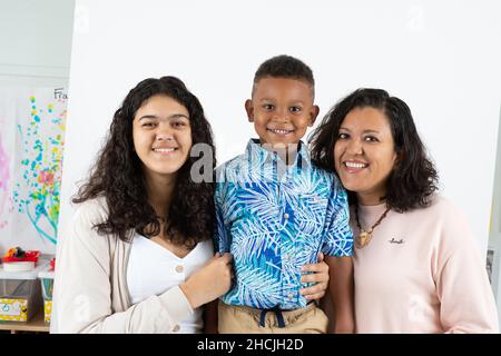 Ritratto closeup di ragazzo di 5 anni, sorridente, sfondo bianco, con madre e sorella di 13 anni Foto Stock